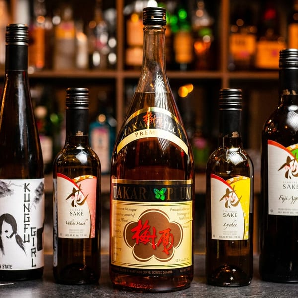 Five bottles of sake and plum wine, with various labels, on a bar counter.