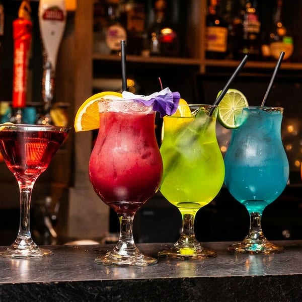 Five colorful cocktails, including a martini and tropical drinks, lined up on a dark bar counter.