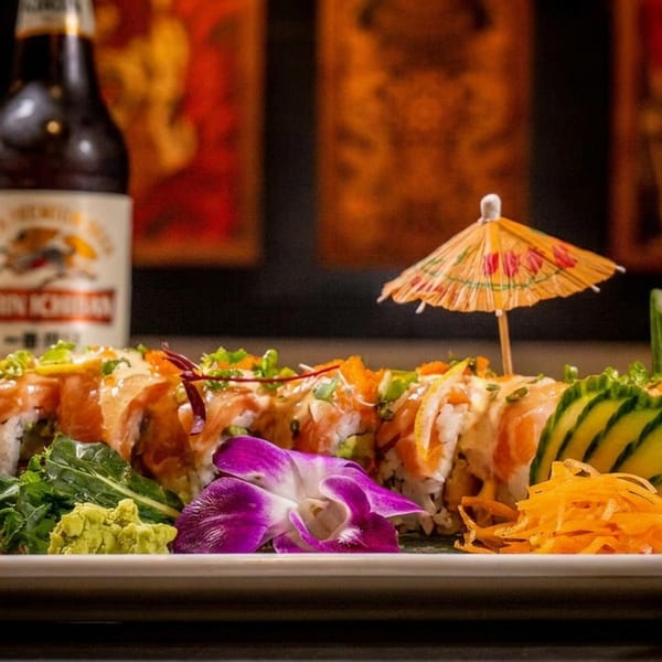 Salmon sushi rolls with garnishes, a purple orchid, and a beer bottle in the background.