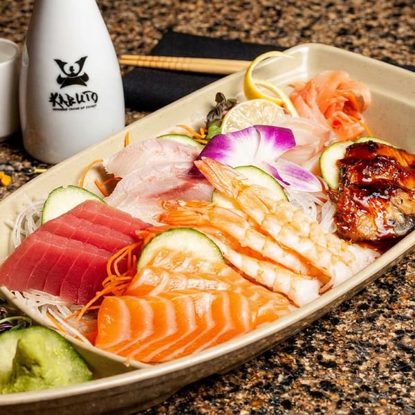 A Kabuto sushi boat with various sashimi, shrimp, and eel, alongside a sake bottle and cup.