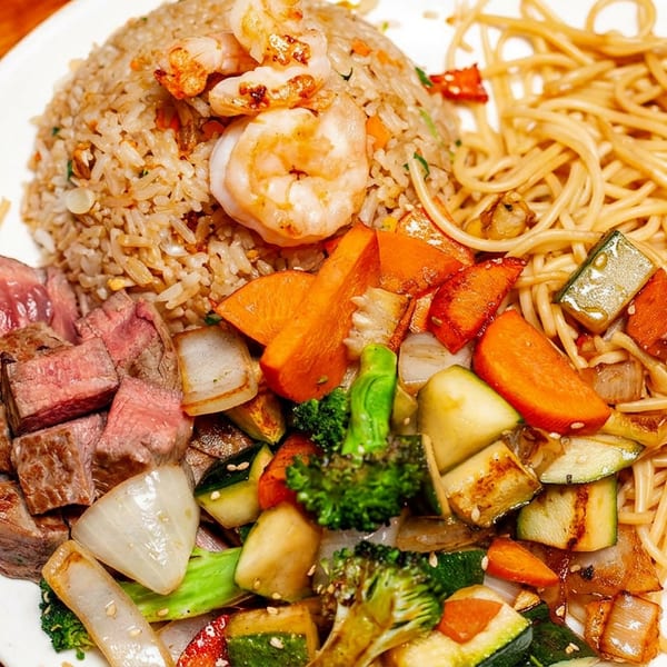 A white plate with steak, shrimp fried rice, noodles, and mixed grilled vegetables.