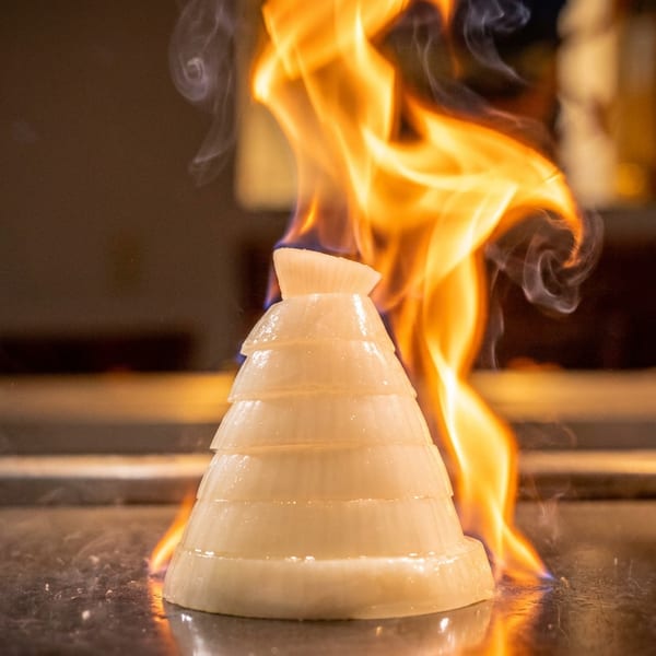 Sliced onion volcano on a hibachi grill with flames shooting up from its center.
