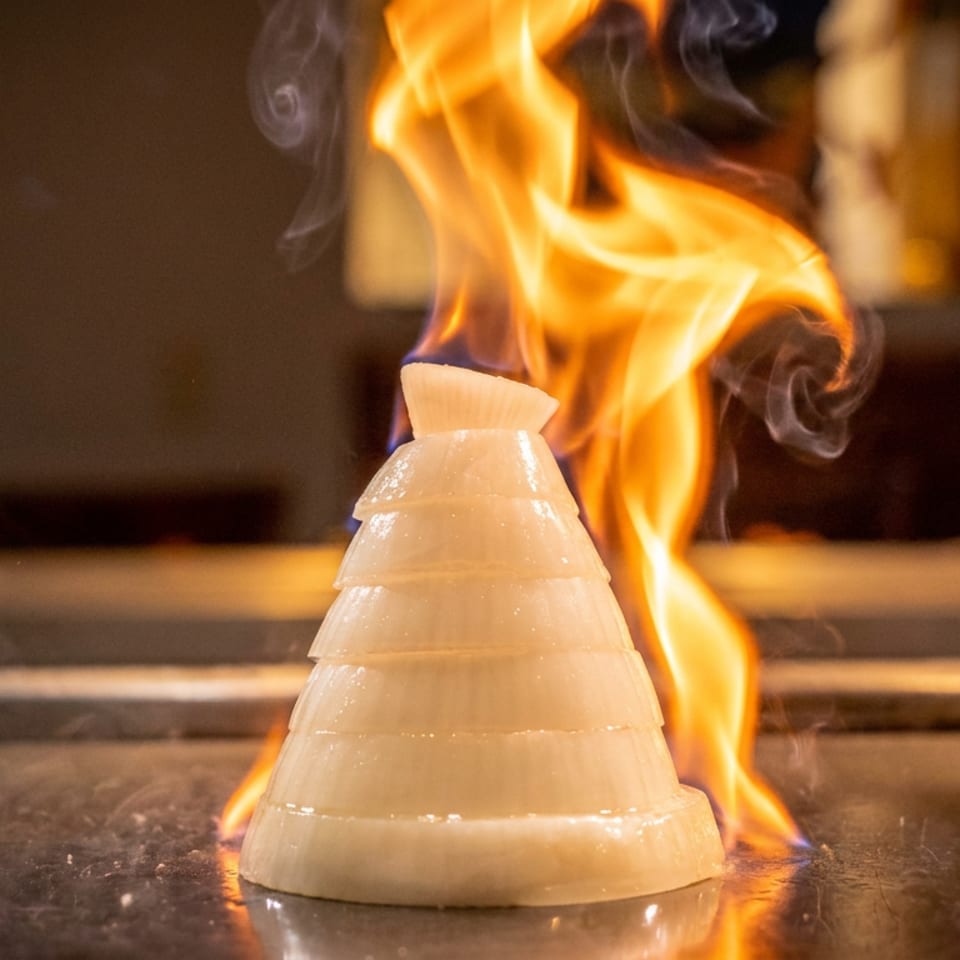 Sliced onion volcano on a hibachi grill with flames shooting up from its center.