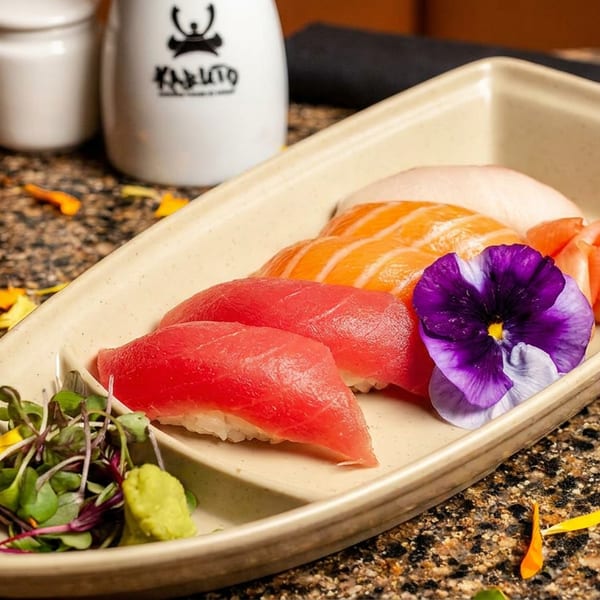 Assorted nigiri sushi with tuna, salmon, and white fish, garnished with a purple flower and microgreens.