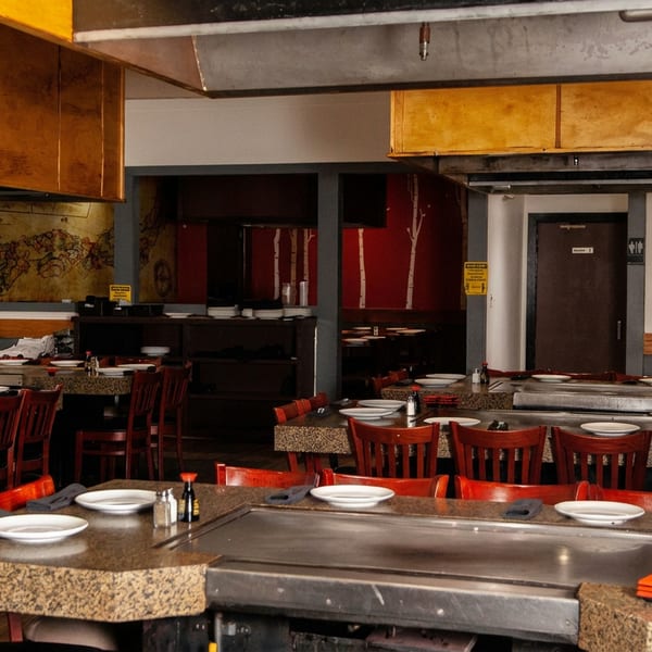 Empty hibachi restaurant dining room with granite tables, red chairs, and cooking griddles.